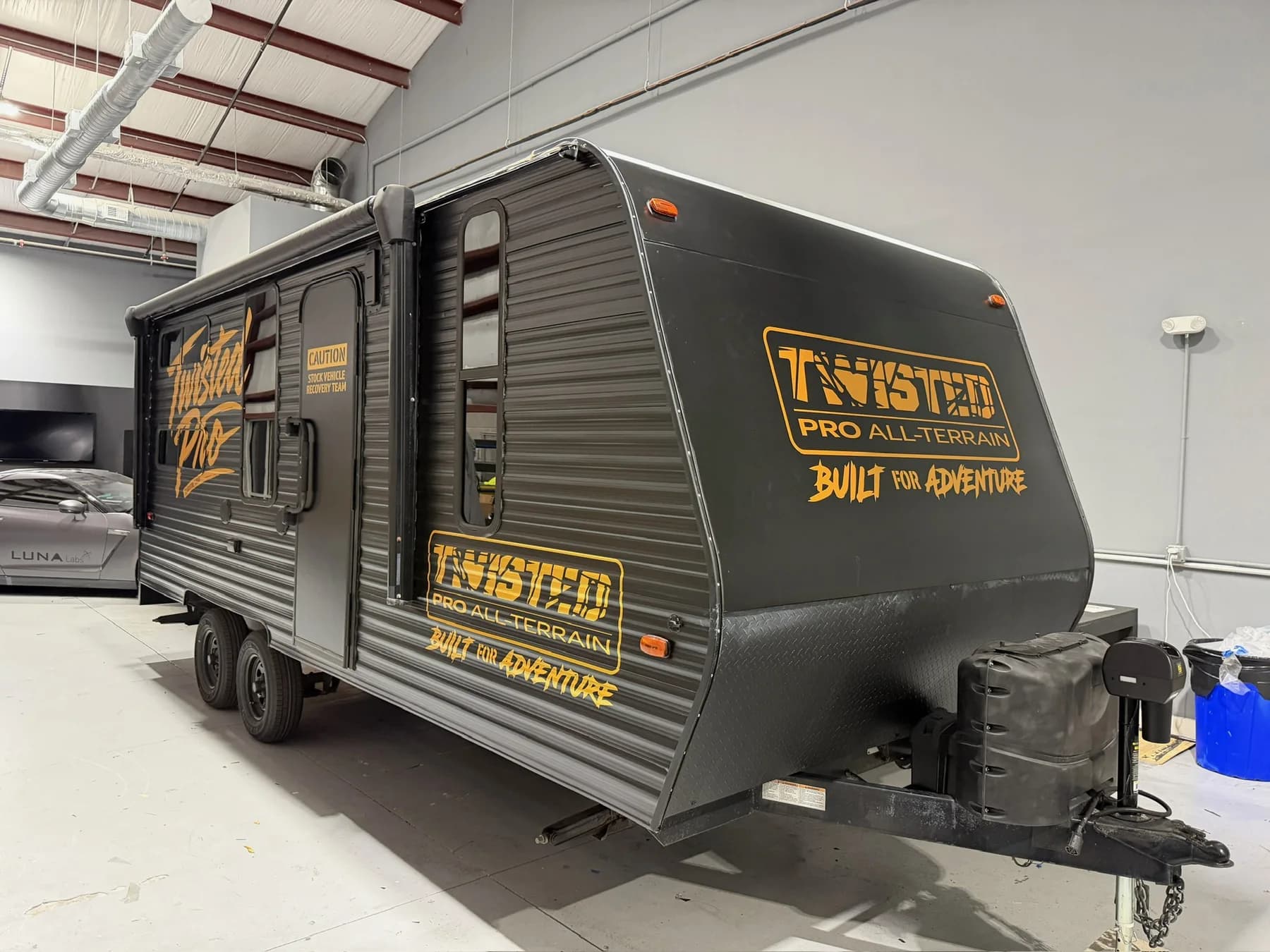 Twisted Pro All-Terrain black travel trailer with yellow commercial graphics